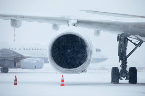 Traffic at airport during heavy snowfall. Snowflakes against jet engine and taxiing airplane at airport taxiway during frosty winter day. Extreme weather in transportation.