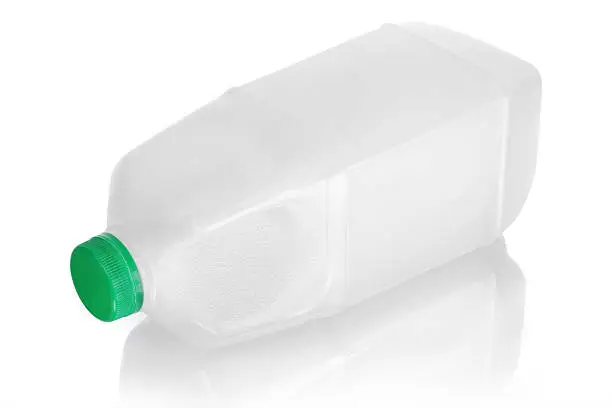 Blank plastic white milk jug isolated on white with green cap. Object laid down on its side.