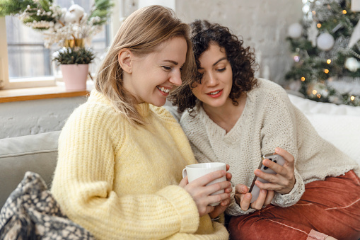 Two young women having coffee and chatting while sitting in a living room