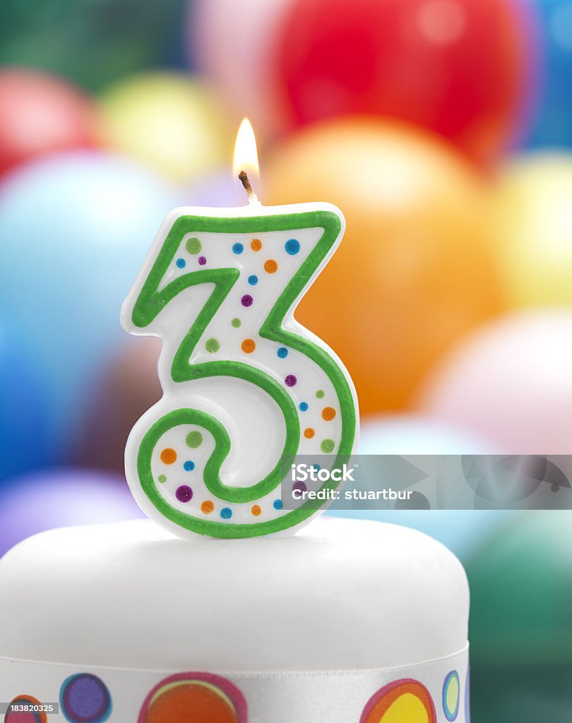 happy 3rd birthday candle as number three on birthday cake with balloons in background Backgrounds Stock Photo