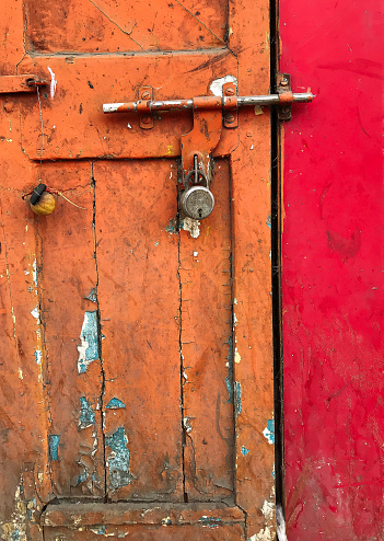 Much used and neglected colorful locked door with flaking, peeling paint, cracked wooden surface and rusty fittings. To evade evil eye lemon, piece of charcoal and chillies are hung on the door.