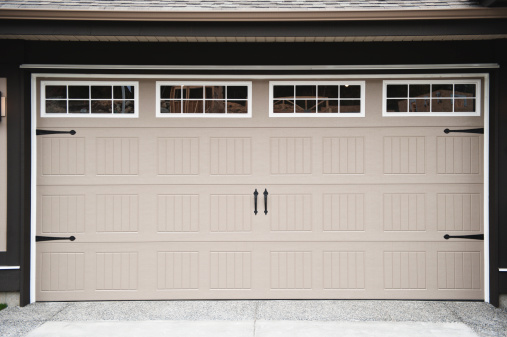 A beige two car garage door with paneled windows along top