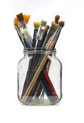 Set of used paintbrushes in glass jar isolated on white background