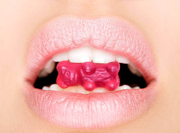 Sweet candy. Close up of female perfectly white healthy teeth biting gummy bear candy. candy in mouth stock pictures, royalty-free photos & images