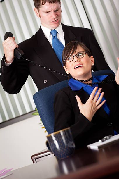 Angry, Jealous Businessman Strangling Business Woman with Phone Cord Color photo of a young business woman being strangled with a telephone cord at her office desk by an angry, jealous coworker. woman strangles man stock pictures, royalty-free photos & images