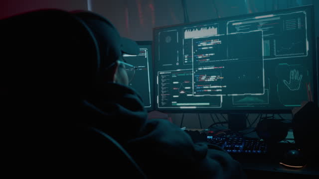 Hacker sitting at table with multiple monitors indoors