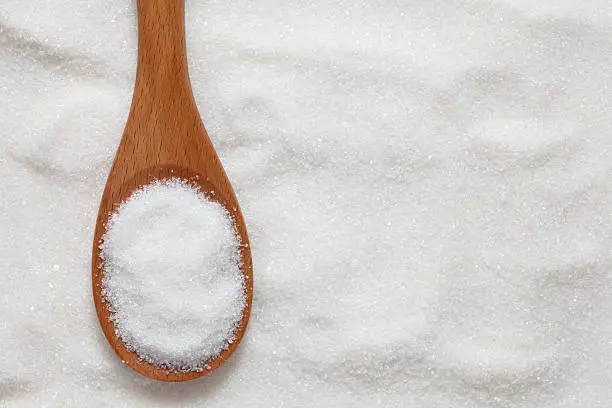 Sugar in a wooden spoon on sugar background. Close-up.Please see: