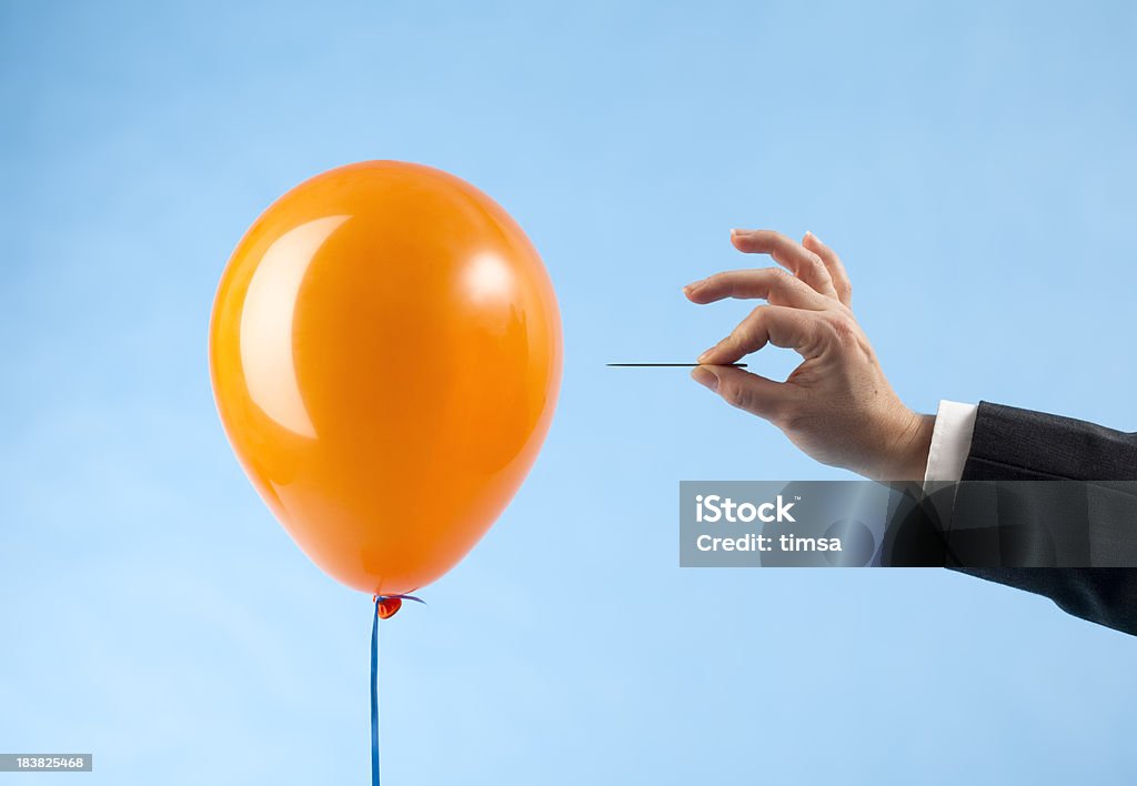 Balloon attacked by hand with needle "Orange balloon and arm in suit approaching it with a needle, ready to burst the bubble. Concept for loss, catastrophic failure. Blue background." Balloon Stock Photo