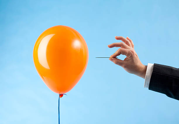 Balloon attacked by hand with needle "Orange balloon and arm in suit approaching it with a needle, ready to burst the bubble. Concept for loss, catastrophic failure. Blue background." sewing needle stock pictures, royalty-free photos & images