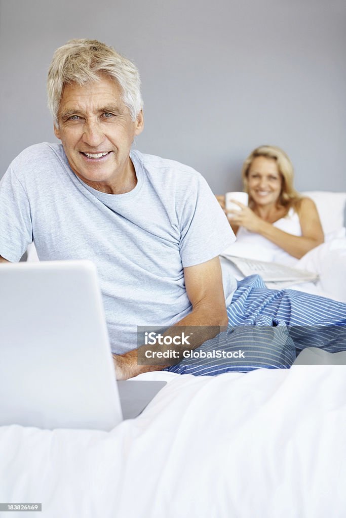 Homme mûr à l'aide d'un ordinateur portable sur lit et souriant - Photo de Adulte libre de droits