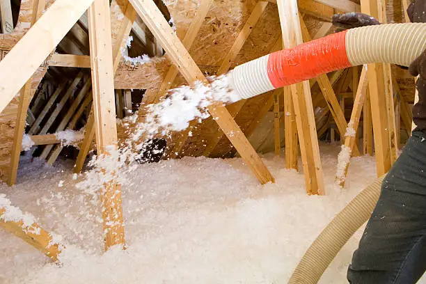 Photo of Worker Spraying Blown Fiberglass Insulation between Attic Trusses