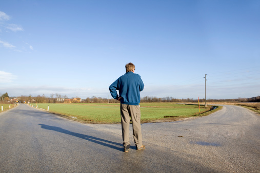 Man standing at the crossroad and deciding which road to take. Can be used in any decision making situation.