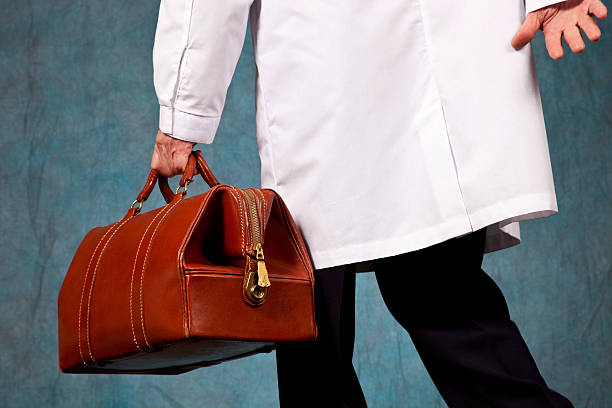 Doctor in lab coat rushing, carrying his leather doctor bag Doctor in white lab coat rushing, carrying his brown leather doctor bag. Rear view. Image shot on blue background with studio strobes, Canon 5D Mark2 , 100 ISO, 24-115mm lens leather medical bag stock pictures, royalty-free photos & images