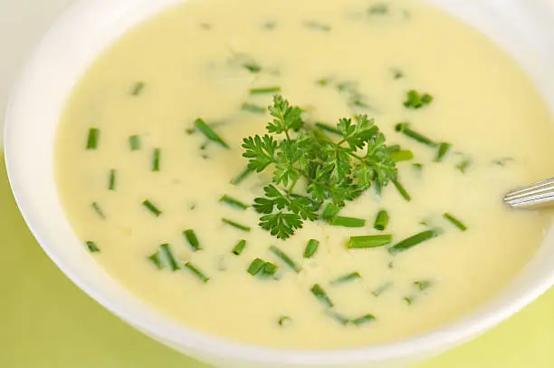 Close-up of white bowl of creamy egg lemon soup with chopped chives and chervil