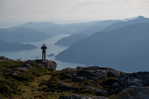Hiker pauses on mountain ridge above coastal mountains and inlet