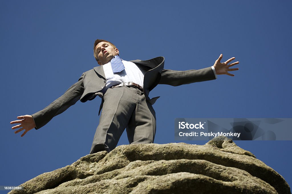 Uomo d'affari saldi sul bordo di una scogliera di roccia - Foto stock royalty-free di Abbigliamento elegante
