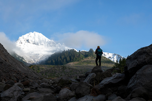 Hiker pauses on ridge below snowcapped mountains and looks out