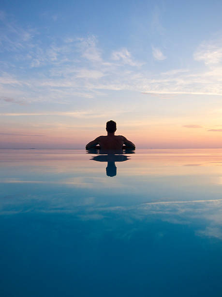 guy riflette in silhouette al tramonto nella piscina a straripamento - infinity pool foto e immagini stock