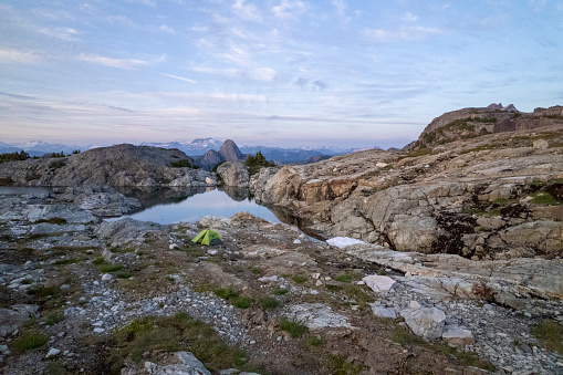 Aerial view of tent camped near alpine lake and mountain ranges distant at dawn