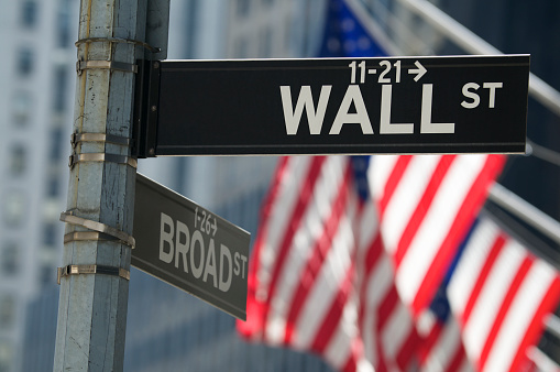 Wall Street sign stands above American flags waving in bright sun