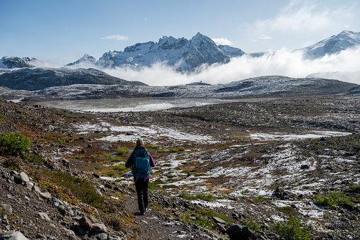 Hiker explores mountain meadow below snowcapped mountains