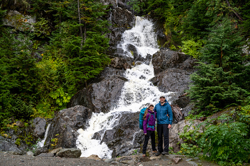 Hiking couple relax in front of waterfall  in lush forest