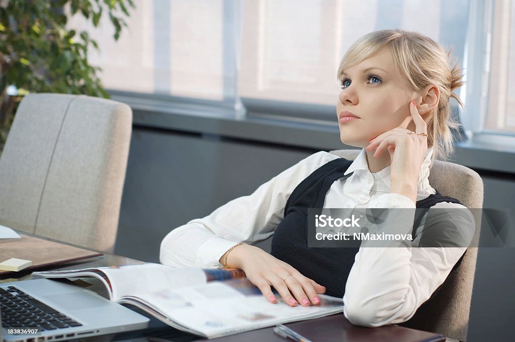 Beautiful businessman in the office Beautiful blonde businesswoman looking up thoughtfully and smiling with laptop and magazine on her office desk. 20-24 Years Stock Photo