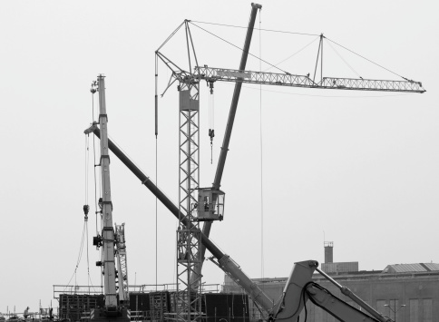 Four cranes and a front end loader at a construction site. Black ans white image.