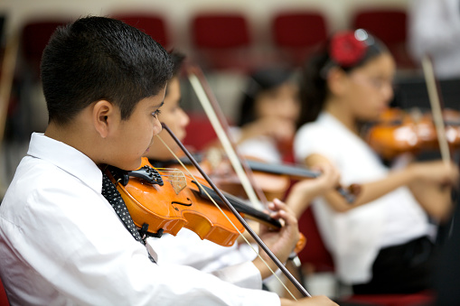 Young violinists play in open concert with the orchestra. Focus on foreground.
