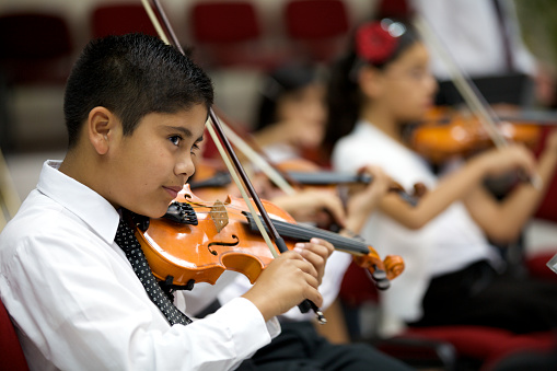 A young boy plays violin and stares outward