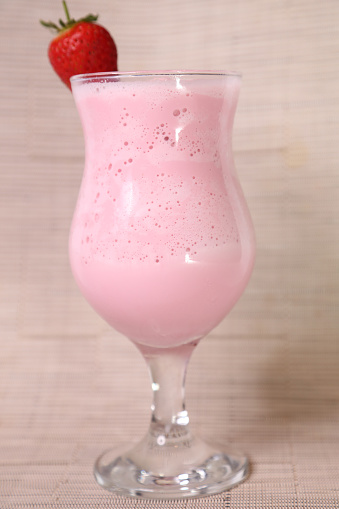 Strawberry milkshake with raw strawberry and straw served in glass isolated on grey background side view of healthy morning arabic drink