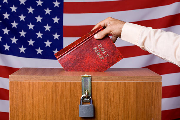 Human Hand Inserting Bible To Ballot Box Before American Flag