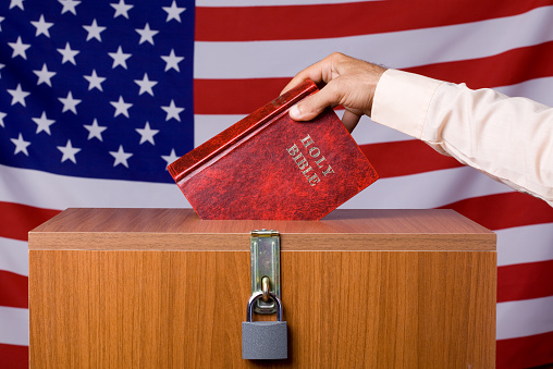 Human hand inserting bible to ballot box before American Flag,The ballot box is locked.The image was shot with a full frame DSLR camera in horizontal composition.