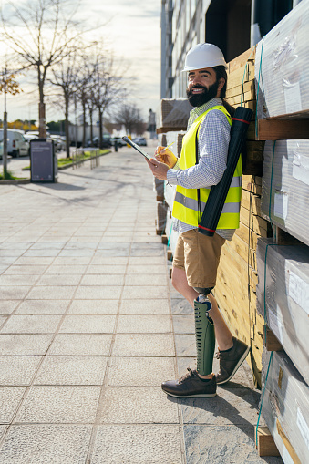 Cheerful bearded inspector with high-vis vest and helmet, noting on clipboard, with visible high-tech prosthetic leg.