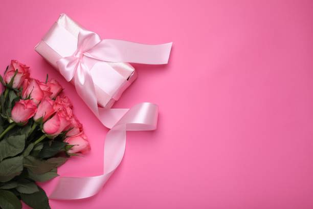 istock Beautiful gift box with bow and roses on pink background, flat lay. Space for text 1838425794