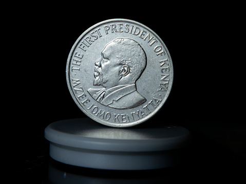 An isolated, silver-colored coin featuring a portrait of a President on the front is shown in the foreground with a plain background