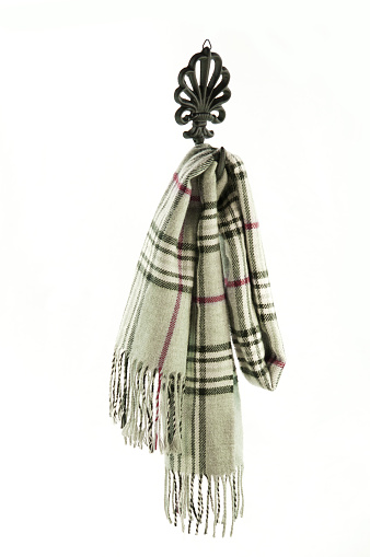 Close-up of a gray plaid scarf hanging on a cast iron hook. White background with copy space.