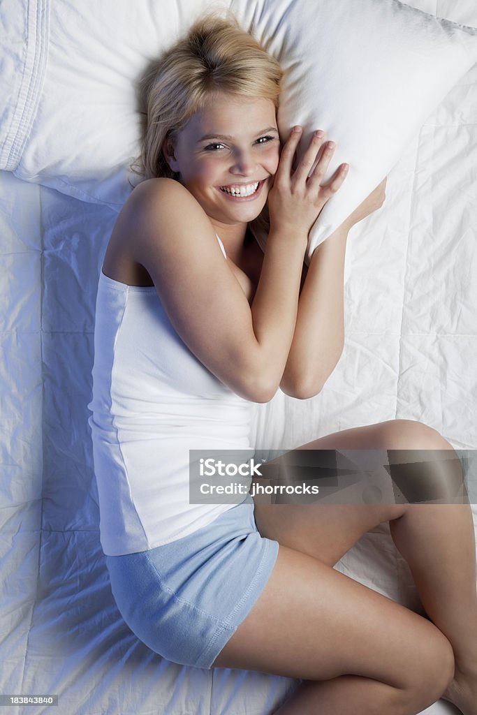 Attractive Young Woman on Bed Photo of an attractive young blonde woman lying on her bed with a bright smile on her face.  Blue lighting effect created with blue gel over studio lighting. Blond Hair Stock Photo