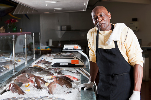 Caucasian fishmonger holding a salmon fillet at a seafood market while facing the camera smiling - People at work concepts