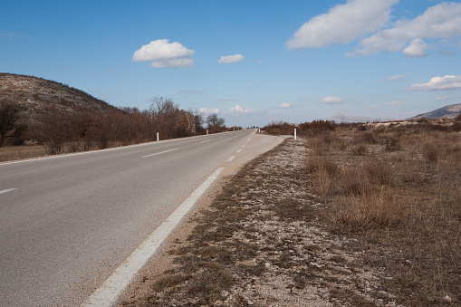 Asphalt road to the horizon, close-up. Background with roadbed and blue sky with white clouds. Traveling by car. High quality photography