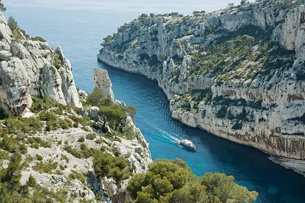 "High angle view of Calanque d'En-Vau on the Mediterranean coast between Cassis and Marseille, France - a narrow inlet whose limestone cliffs rise above a tour boat in the lower right."