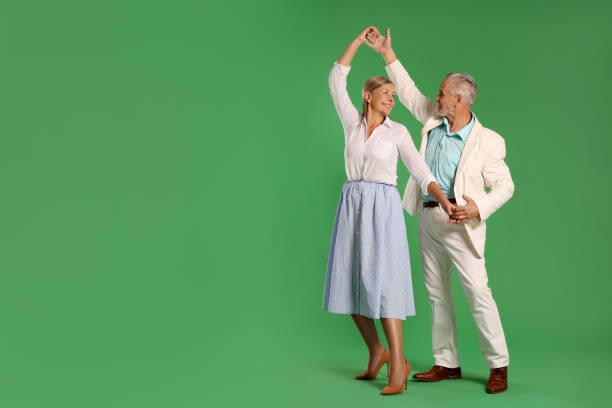 Senior couple dancing together on green background, space for text