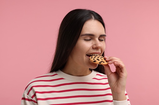 Young woman with chocolate chip cookie on pink background