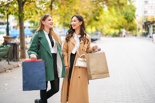two young women shopping are walking on the big street and looking at the stores