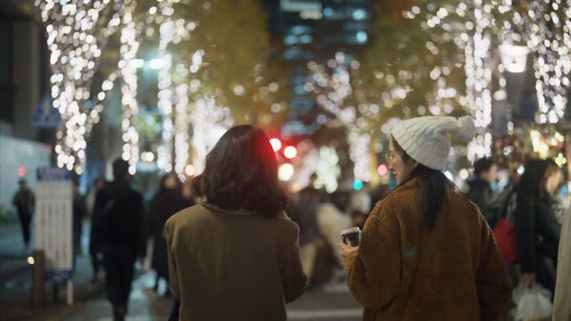 Back view of happy Asian woman walking and interested in beautiful city at night with many Christmas lights.