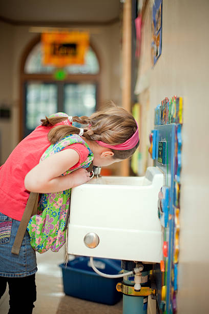 Girl Student Drinking from Fountain at School An elementary aged girl takes a break from class for a drink of water at a drinking fountain in her school hallway.  Vertical with copy space. drinking fountain stock pictures, royalty-free photos & images