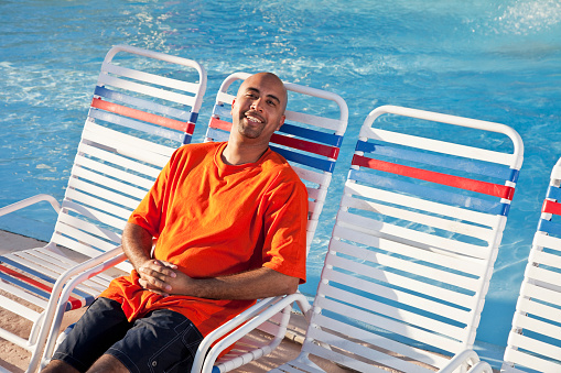 African American man, 40s, sitting on lounge chair by swimming pool