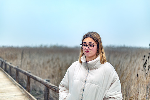 Laguna de Manjavacas, Mota del Cuervo, Castilla La Mancha, Spain.Young woman with glasses and winter clothing displaying an indifferent gesture in a minimalist rural environment with fog.
Half-body view of a man with his back turned, looking at wind turbine towers next to a sunlit tree.