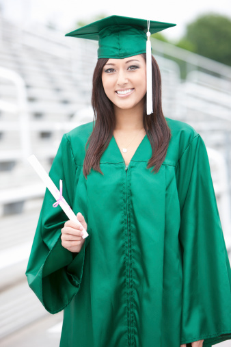Beautiful Asian teenage girl holds up her diploma in her graduation gown. Outdoor portrait in empty school bleachers. CLICK FOR SIMILAR IMAGES AND LIGHTBOXES WITH EDUCATION IMAGES OR ETHNIC FACES.