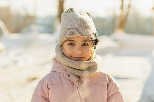 Blonde girl in winter jacket and hat outdoors.